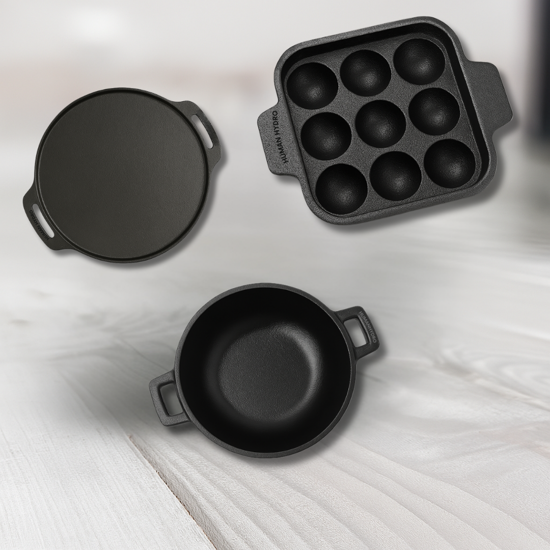 A collection of three cast iron cookware pieces: a skillet, an egg cooker, and a small round pot on a wooden surface.