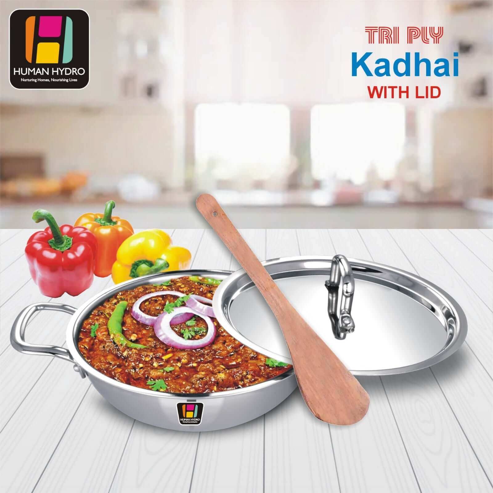 Tri-ply stainless steel kadai with lid, wooden spatula, and colorful bell peppers on display for cooking.