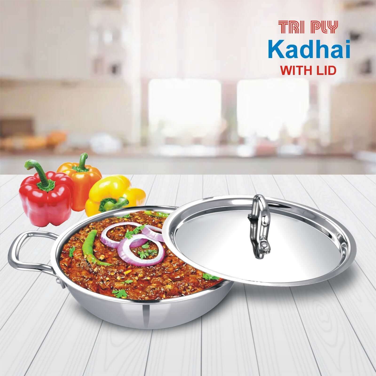 Tri-ply stainless steel kadai with lid, filled with curry, placed on a kitchen counter, showcasing cookware.
